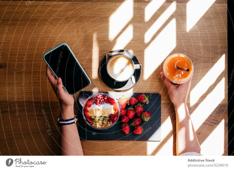 Woman having healthy breakfast and using phone woman healthy food smartphone table strawberry smoothie bowl fruit coffee wooden juice female mobile cellphone