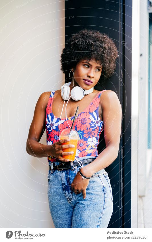 Charming black woman with cup of juice healthy drink dream colorful style young casual african american takeaway headphones thoughtful plastic female pensive