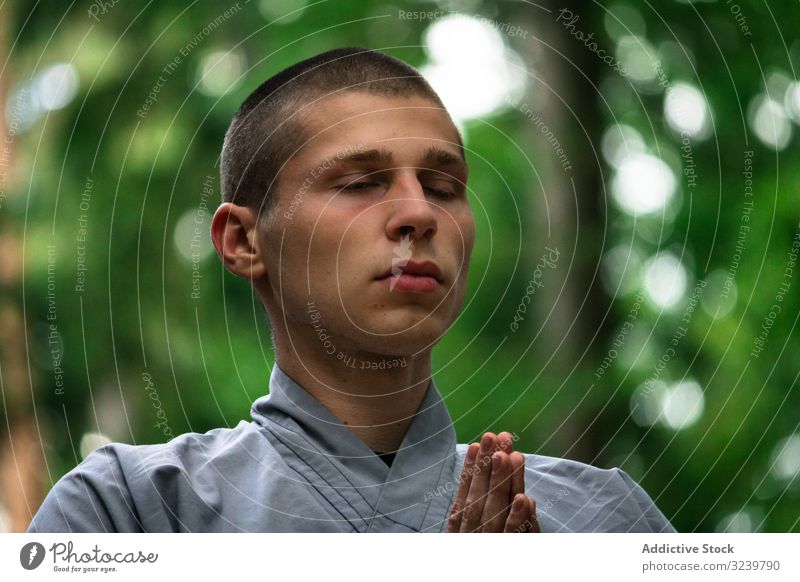 Young man meditating in garden martial training meditation clasped hands taiji retreat exercise uniform practice male bald focused serious concentrated workout