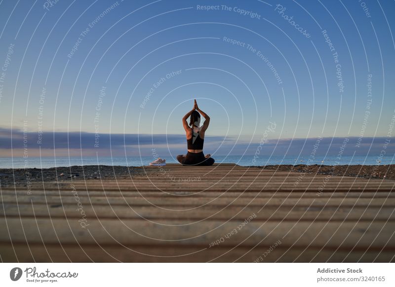 Adult woman meditating near sea in evening yoga beach asana activity fit clasped hands crossed legs sky cloudy female positive smile slim sportswear training