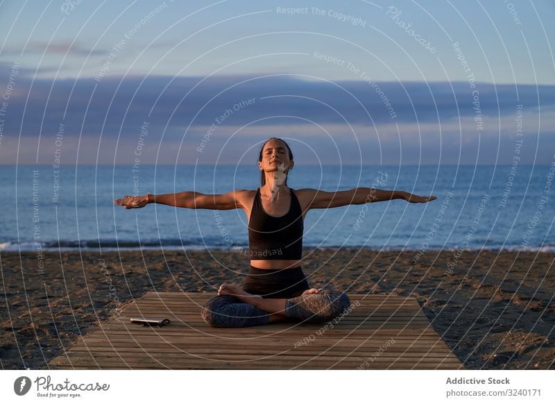 Adult woman meditating near sea in evening yoga beach asana activity fit crossed legs sky cloudy female positive sportswear training workout fitness pose