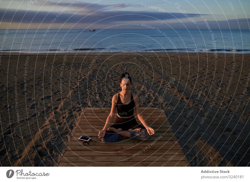 Barefoot woman meditating on wooden path yoga beach asana activity lotus pose fit closed eyes crossed legs female slim sportswear training workout fitness