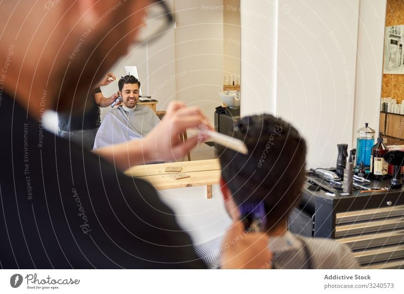 reflection in the mirror of a barber cutting hair with a machine to a customer sitting on the barber chair reflexion shaver barbershop comb hairstyle furniture