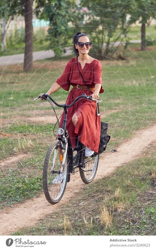 Woman riding bicycle in park woman path smile casual city summer activity female bike vehicle transport lifestyle rest relax weekend cheerful lady dress