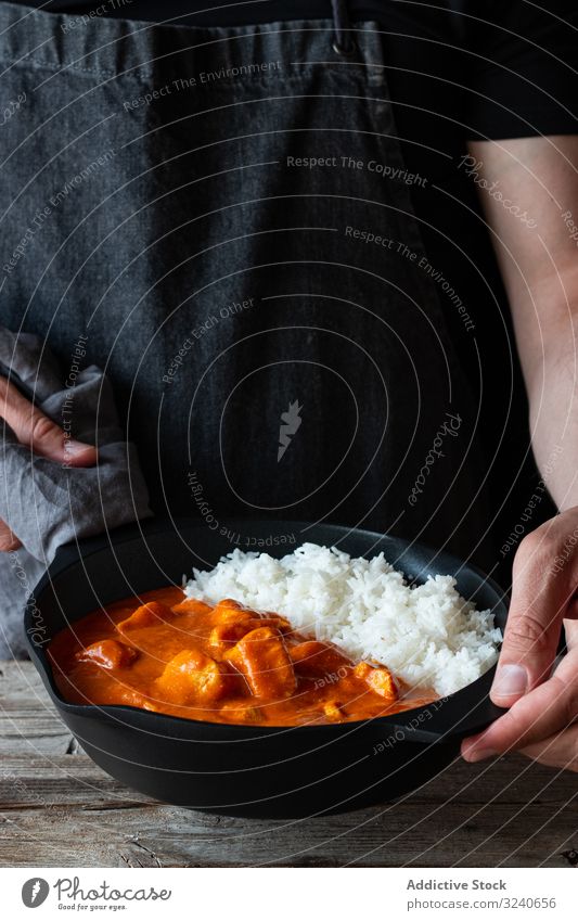 Faceless cook holding frying pan with hot butter chicken rice food dish indian cuisine curry basmati delicious gourmet traditional asian tasty meal person