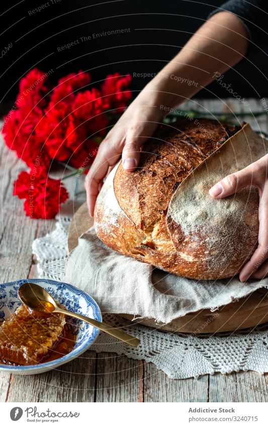 Crop person putting sourdough bread near flowers and honey table fresh loaf meal food honeycomb baked rustic napkin crust crunchy kitchen bouquet carnation