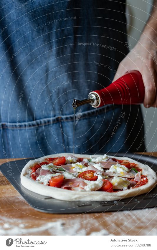 Crop chef pouring oil on pizza man dough flour soft fresh cuisine kitchen preparation meat food cheese tomato ham sauce spill add italian male apron raw