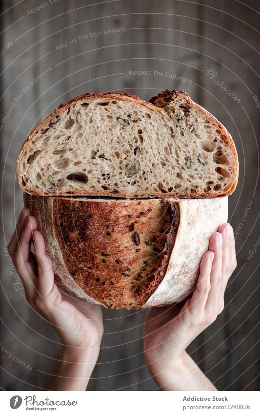 Crop person holding halved seeded bread fresh half show meal food wall cuisine kitchen home snack rustic baked scrumptious demonstrate cut healthy divided