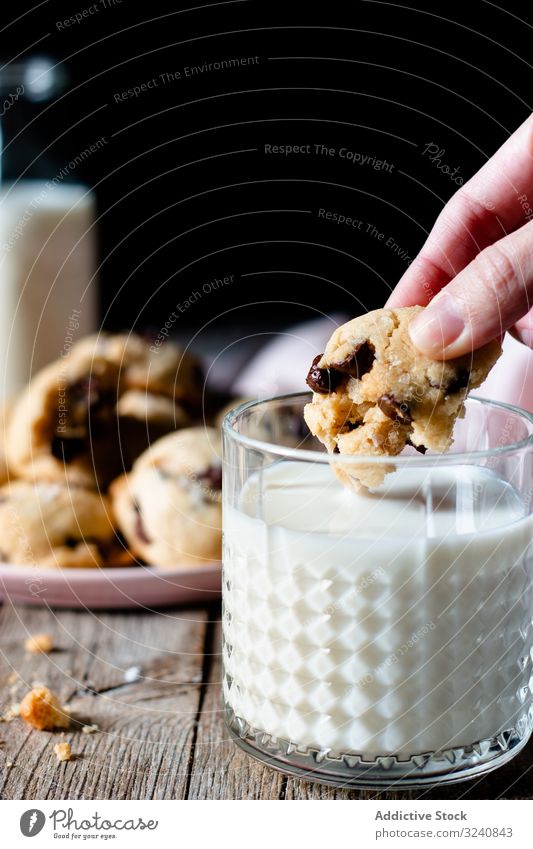 Crop woman dipping vegan cookie with chocolate chips into milk piece glass home drink beverage food edible meal tasty delicious yummy dairy vegetarian dessert