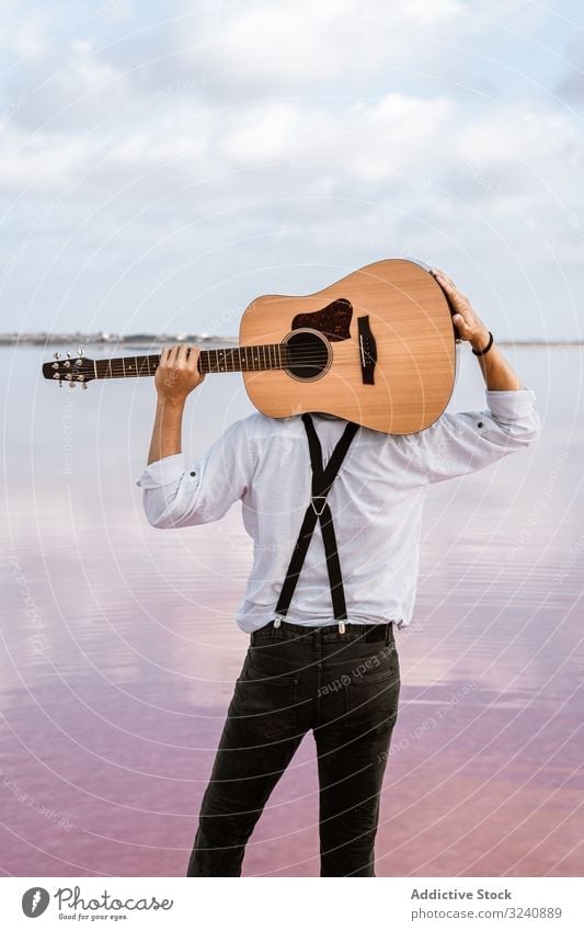 Musician gazing and carrying guitar behind back while standing on beach musician gaze man acoustic new modern usa hold shore young adult white shirt waterfront