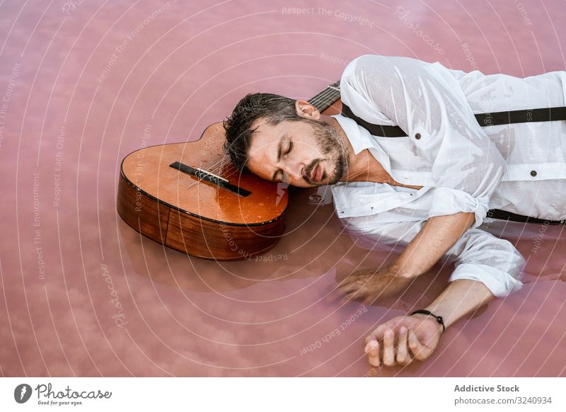 Man resting in water with guitar at seaside man classy lying down floating sandbank white shirt suspenders dreamy peaceful calm neutral young adult bristle