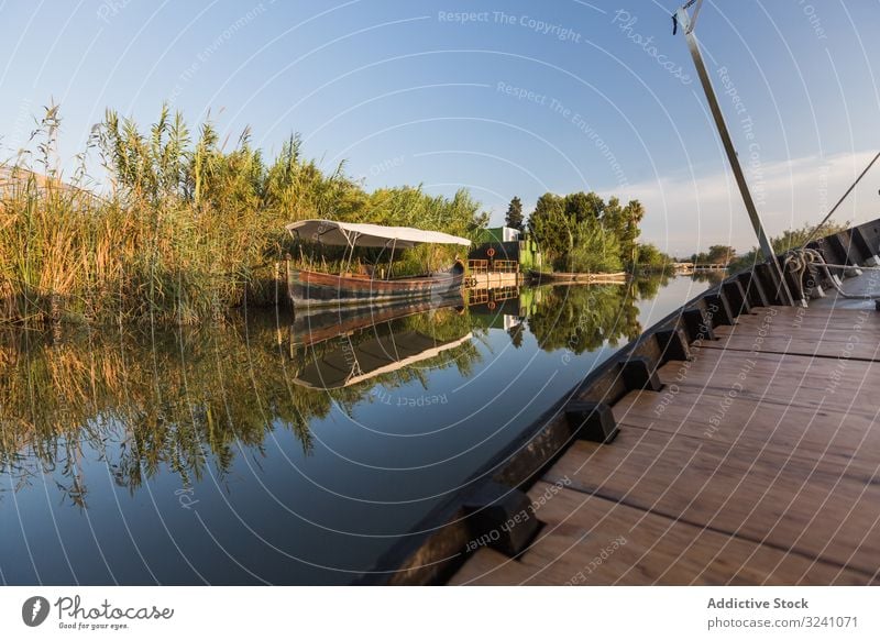 Side of modern boat sailing along rural shore vessel ride tranquil sunny coast lagoon valencia reflection smooth waterfront greenery side detail wooden new
