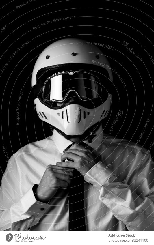 Stylish driver in helmet and eyeglasses adjusting tie in studio man racer white shirt goggle elegant extreme contrast equipment transportation headgear formal