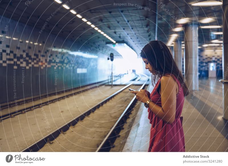 Long haired woman with smartphone standing in front of subway car waiting using stop urban platform underground browsing surfing budapest hungary gadget device