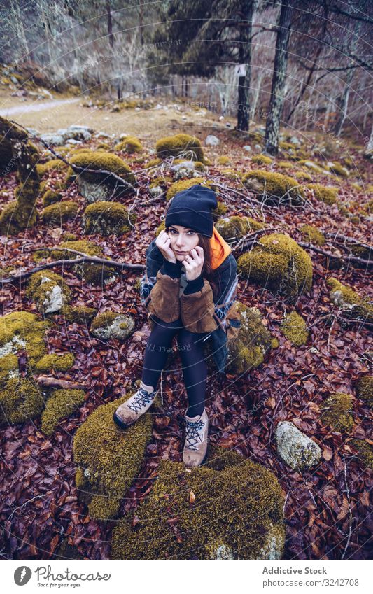 Bored female tourist resting on rock at autumn forest bored sit stone woman dried foliage brown moss leaning on hand hat neutral calm serious young adult sad