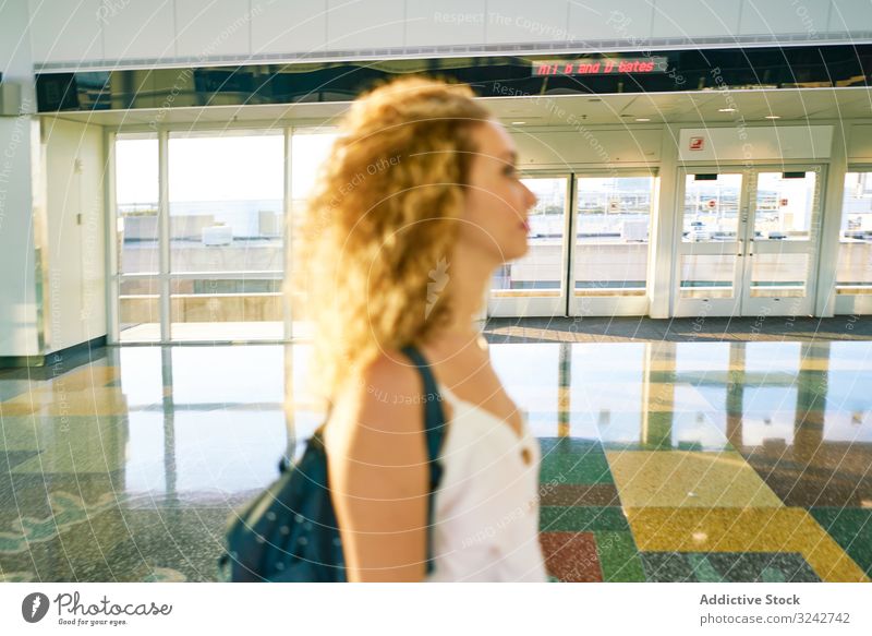 Thoughtful woman walking in spacious hall in sunlight airport interior marble glass modern lobby design flight travel shine gate international female casual