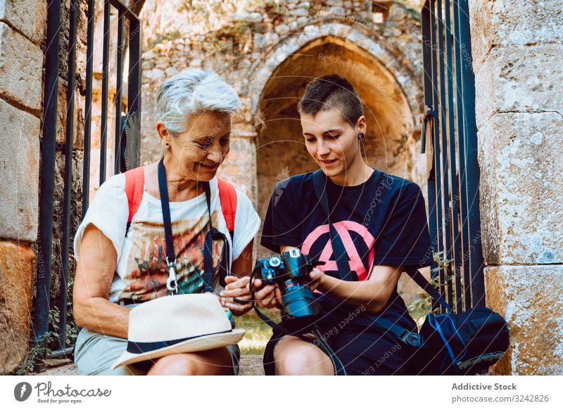 Stylish young woman showing photography to mature lady on stony steps women watching camera vacation summer photographing memory grandmother granddaughter happy