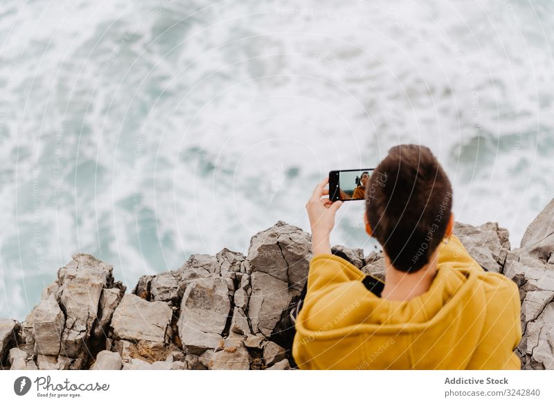 Woman in yellow hoodie taking selfie on smartphone on rocky shore woman solitude alone contemplation stone ocean pensive using relaxation freedom coast lonely