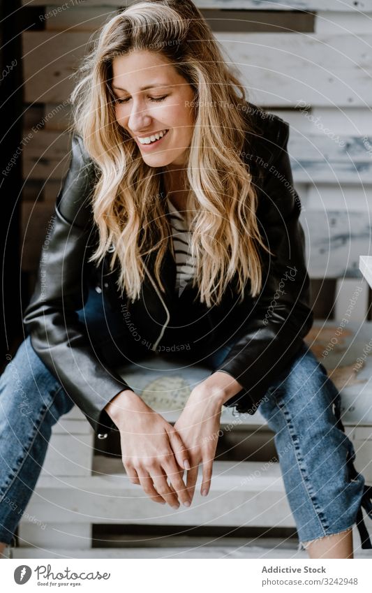 Woman sitting in a wooden bench in cafe woman stylish blonde waiting design trendy creative clothing leather jacket casual denim bright curly model female vogue