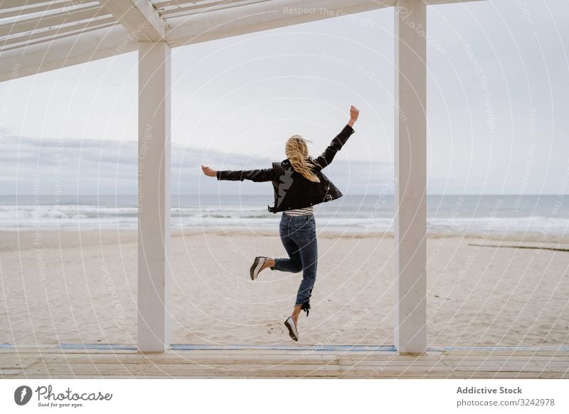 Joyful woman jumping raising hands up on wooden beach pier happy energy trendy arms raised excitement coast freedom inspiration ocean shore travel carefree