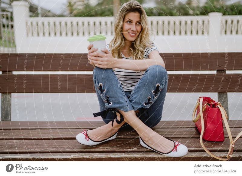 Happy woman with disposable cup of coffee sitting on street bench city seafront happy joyful enjoy casual rest young female laugh smile excited beautiful drink