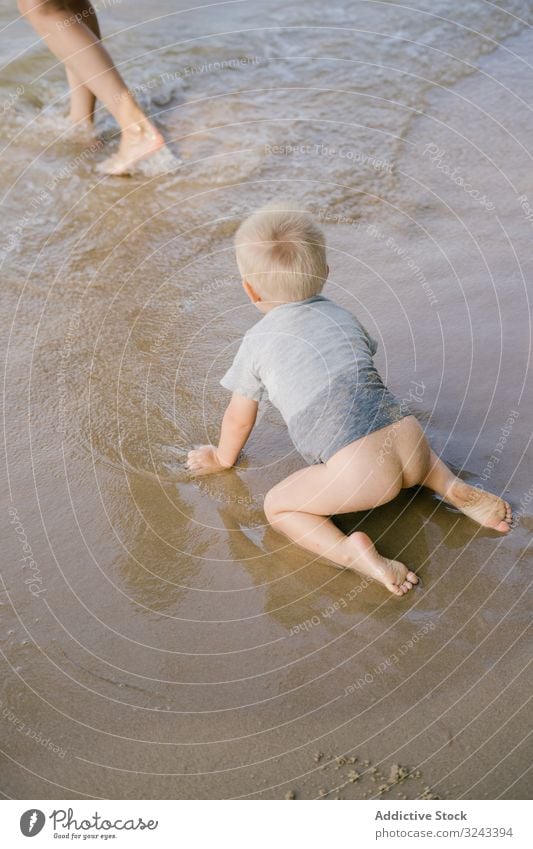 Small kid with undressed bottom crawling on wet sandy beach water mother curious tropical swim on all fours childhood ocean son seascape nature relax boy