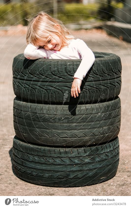 Little girl resting in stack of tires kid naughty fun play prank tyre little happy joy child childhood active cheerful leisure smile laugh game hide hole joke