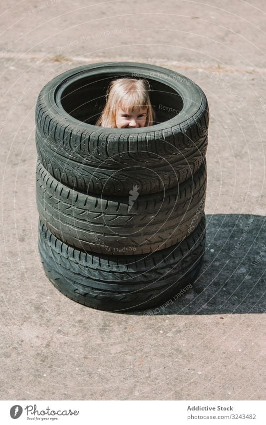 Little girl hiding inside stack of tires kid naughty fun play prank tyre little happy joy child childhood active cheerful leisure smile laugh game hide hole