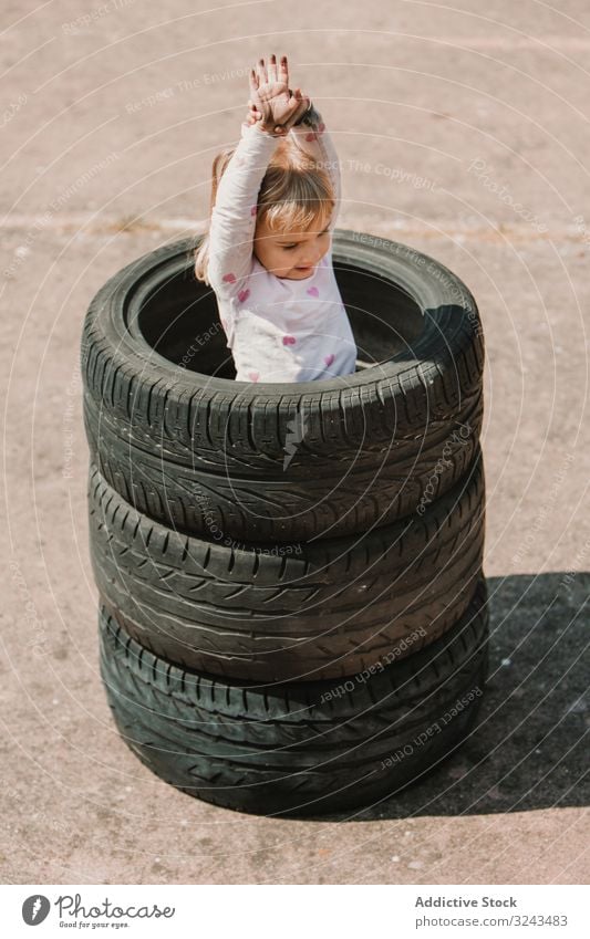 Little girl standing in stack of tires kid naughty fun play prank tyre little happy joy child childhood active cheerful leisure smile laugh game hide hole joke