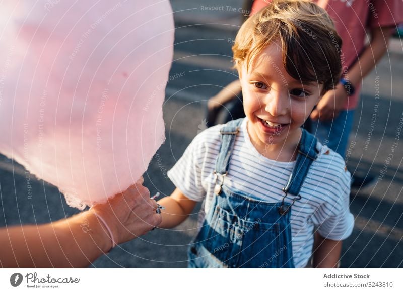 Cheerful boy taking candyfloss from vendor funfair excited smile street city sweet seller kid child joy happy urban town cotton candy casual delighted