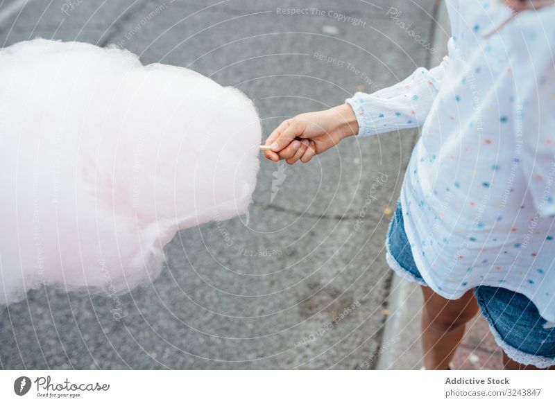 Cheerful girl eating cotton candy on street candyfloss stall smile city fair joy kid happy child urban town sweet fun vendor buy sell sidewalk pavement casual