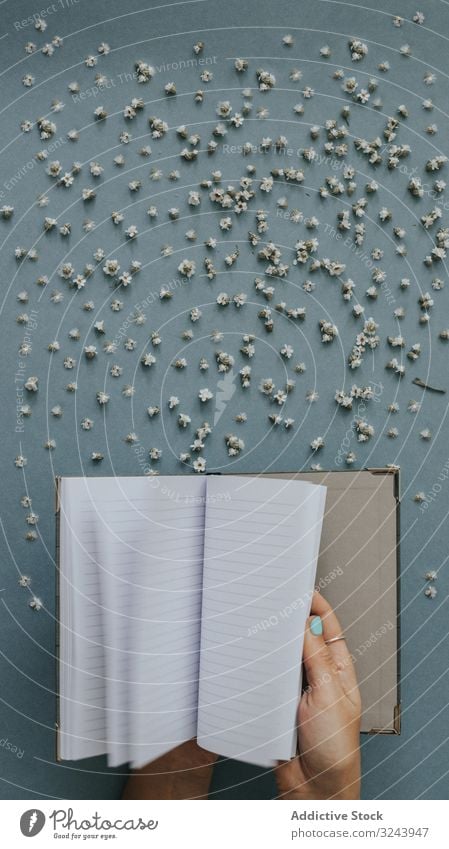 Person flipping blank notebook on blue background with tiny flowers around message empty paper scatter design fly concept write piece white page memo template