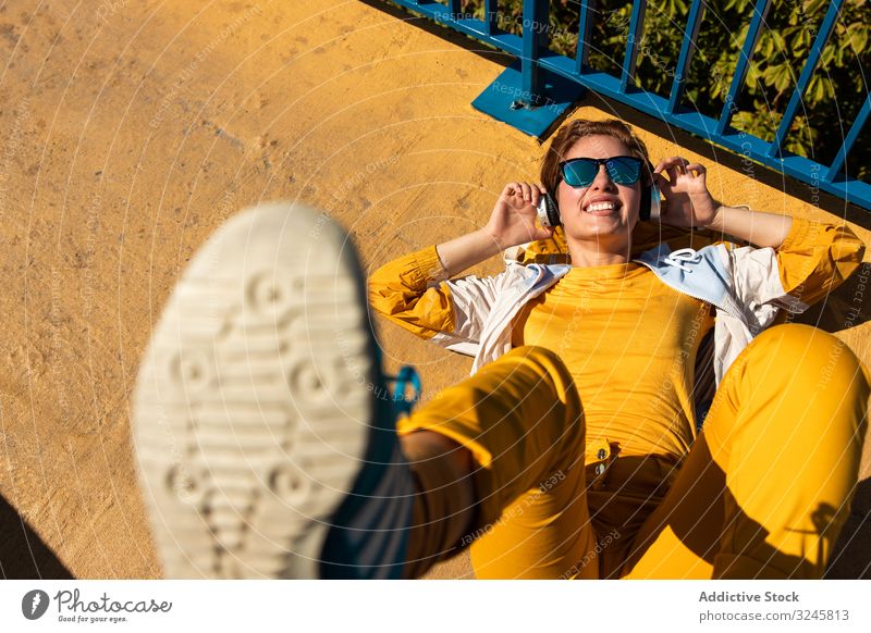 Stylish young woman in vibrant clothes enjoying music on street headphones colorful yellow urban bright blue millennial trendy chill sunglasses music lover