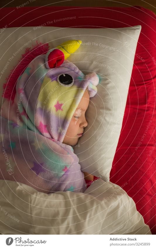 Girl in unicorn pajama sleeping in bed kid child kigurumi girl blanket red white dream lying cute little childhood night bedtime home relax pillow rest adorable