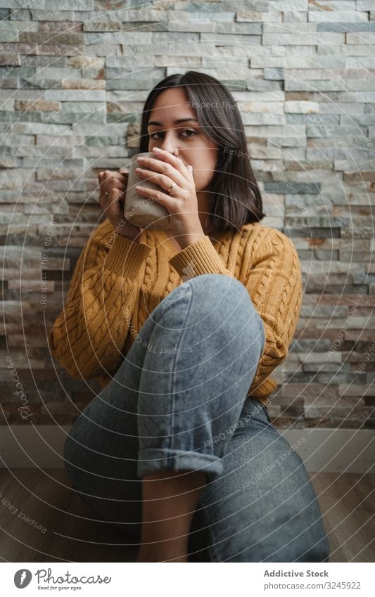Woman drinking hot tea at home woman mug sweater coffee sit floor jeans female cup beverage young hold relax enjoy recreation warm up cold pullover room house