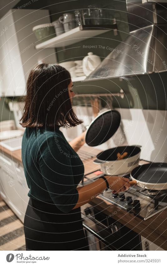 Woman opening lid of pan in kitchen woman stove cooking pot house preparing home checking young female brunette casual hold stand household homey food homemade