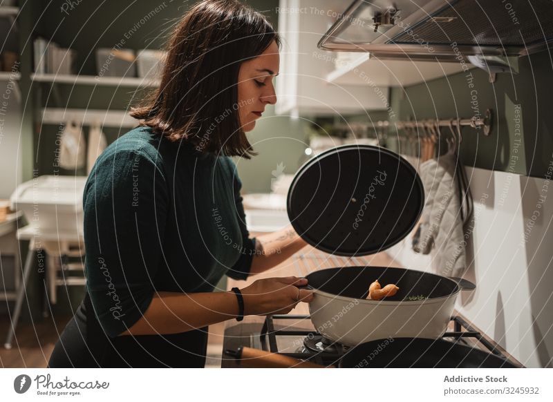 Woman opening lid of pan in kitchen woman stove cooking pot house preparing home checking young female brunette casual hold stand household homey food homemade