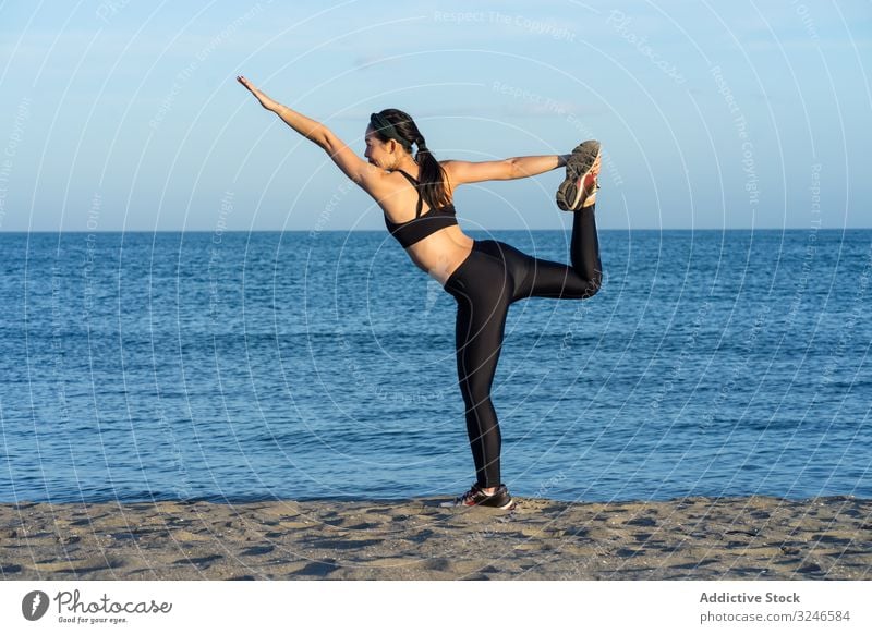 Content sportswoman in active wear doing yoga at seashore posture pose attitude beach ocean blue sky workout fit young sportswear training female action