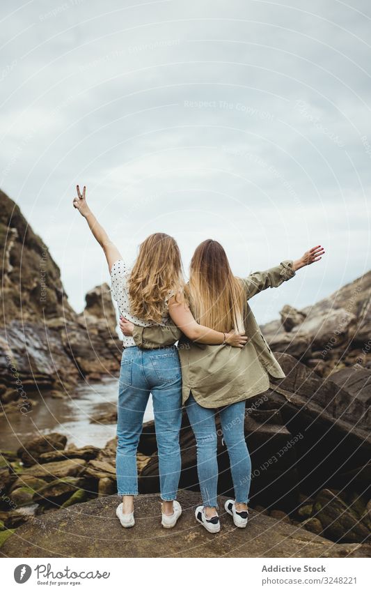 Young sisters standing on stone on spring day women embrace nature hill mountain countryside together female friends love hug support friendship relationship