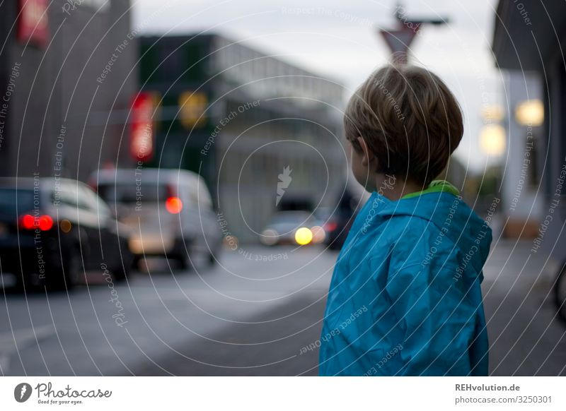 Boy stands by the road Dreary Bad weather clearer Light Passenger traffic Means of transport Downtown Vehicle Crossroads Colour photo Pedestrian Motoring