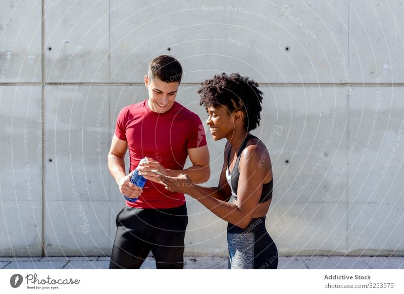 Multiracial sportive couple having break and using smartphone sportspeople city together rest happy share smile building wall mobile water bottle exercise