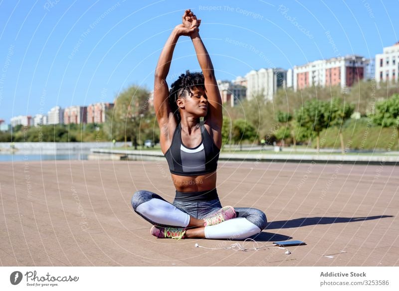 African American sportive woman sitting in lotus pose and stretching hands up lotus position sportswoman city rest recreation practice relaxation yoga zen asana