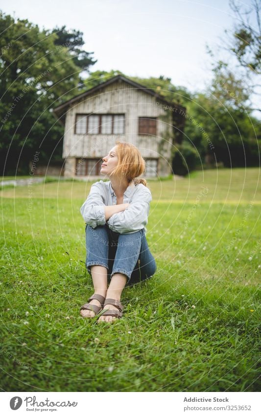 Content female sitting on grass in countryside woman house enjoy field meadow calm peaceful content thoughtful carefree rural village redhead ginger walk scenic