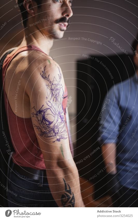 Man looking at tattoo sketch on arm in salon man template drawing check contemplate art careful serious thoughtful focused artwork skin body modern professional