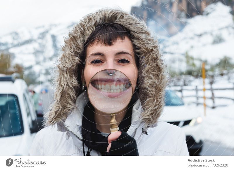 Woman smiling through magnifier in winter woman teeth smile interested road countryside mountain snow empty piercing content playful laugh female white curious