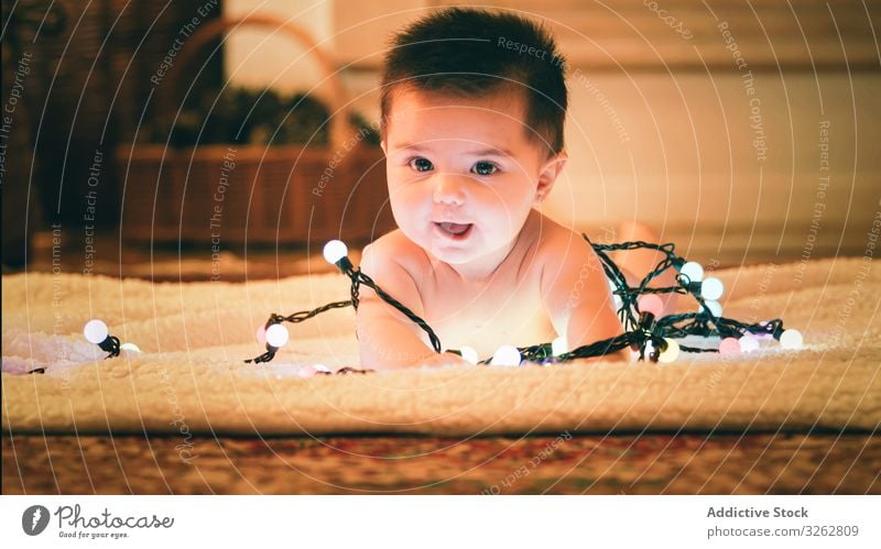 Baby playing with light garland on Christmas Day baby christmas colorful cozy evening carpet floor cute adorable child kid happy joy holiday winter december