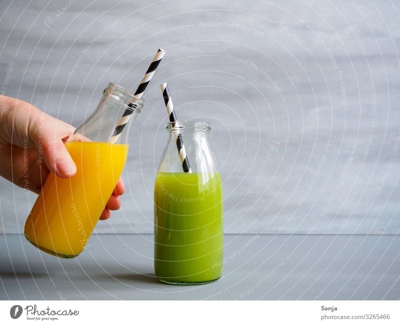 Hand with Orange Juice and Green Smoothie Breakfast Diet Beverage Orange juice Bottle Glass Lifestyle Healthy Wellness Well-being Feminine Woman Adults Fingers