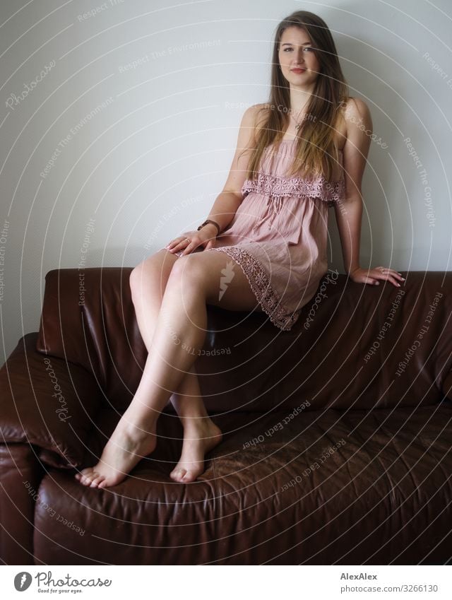 Portrait of a young woman on a brown couch Elegant Style Joy already Life Sofa Room Young woman Youth (Young adults) Legs 18 - 30 years Adults Dress Barefoot