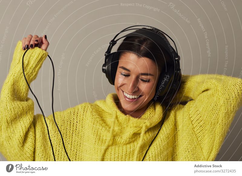 Playful young woman listening to music in studio headphone wear yellow sweater enjoy stereo playful female fun using sound playlist connection relax pleasure