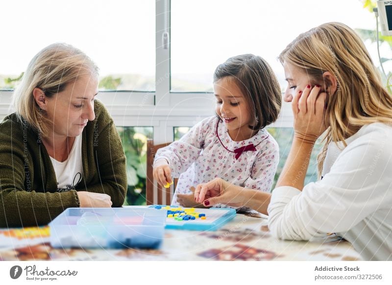 Woman playing board game with daughter and granddaughter family multi generational mother daughters together fun happy grandmother woman girl table piece female